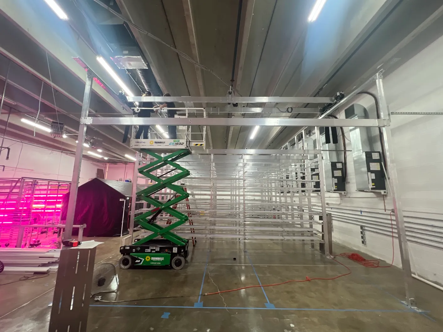Installing the overhead gantry frame in a vertical-farm facility — the rail structure the robot travels on, going up over the grow racks.