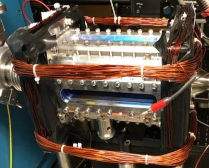 The interaction chamber wrapped in its magnetic-field coils, molecular fluorescence glowing through the viewports.
