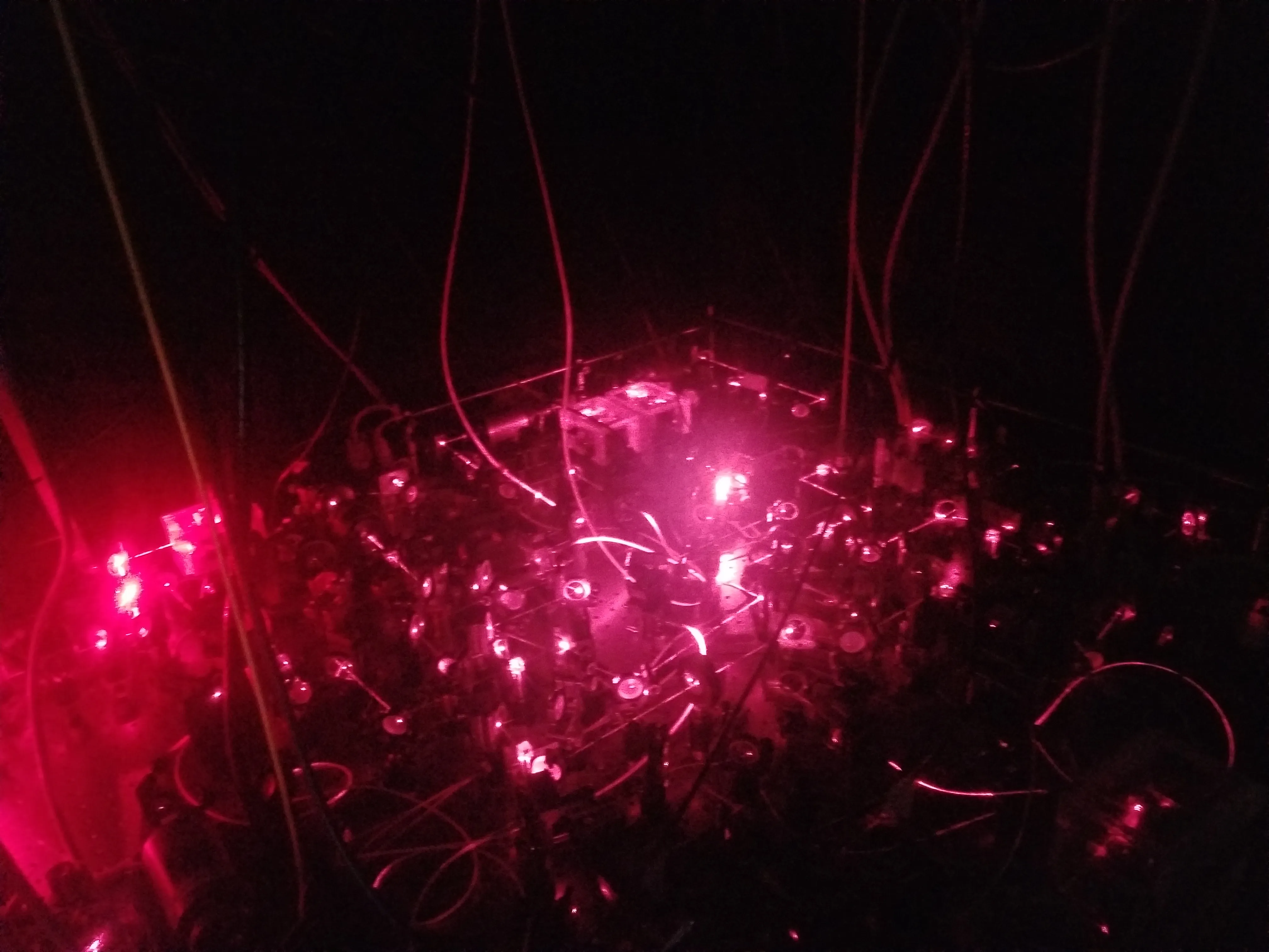 The molecular-cooling laser table in operation, lit by 635 nm light — the free-space optical system I built and ran.