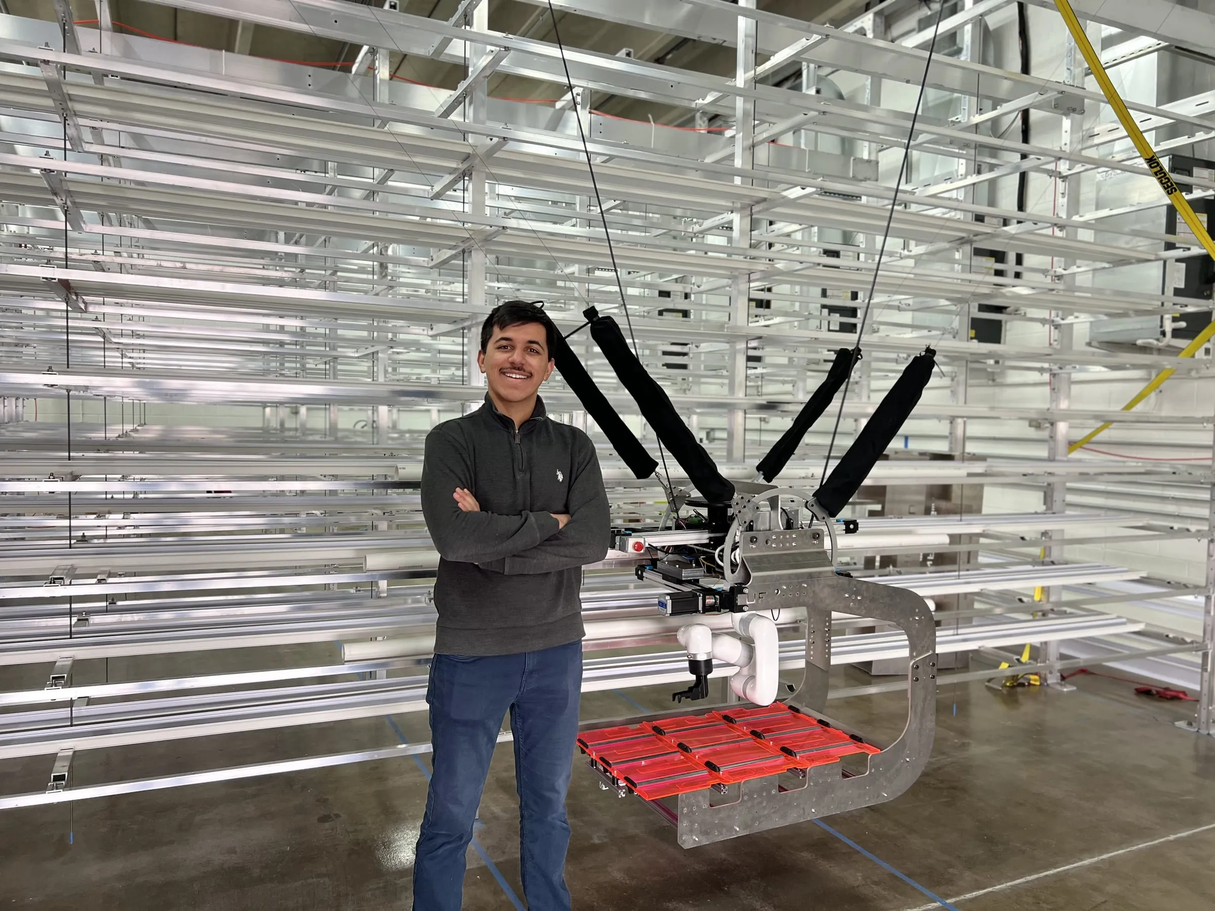 The finished cable-suspended gantry robot in front of the racks it services, with the tray-handling end effector on its arm.